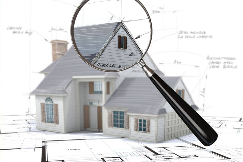 A magnifying glass is held over a picture of a home to highlight parts of a home inspection